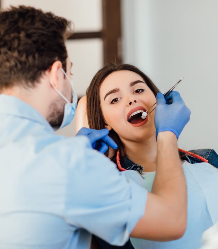 Dentist making professional teeth cleaning withb the cotton, female young patient at the dental office.